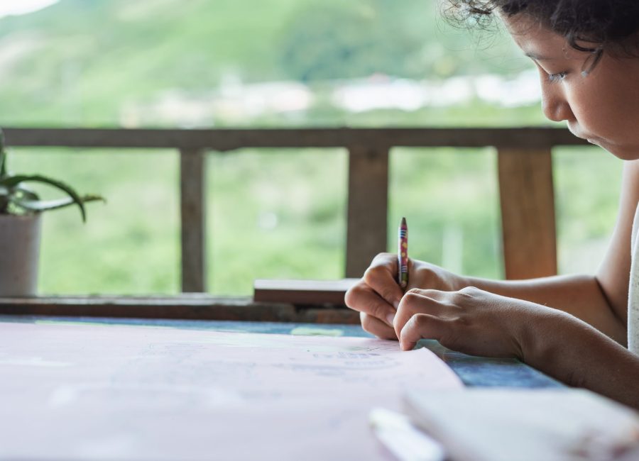 brown-skinned, low-income latina student doing her school homework at home. girl drawing a picture on a large pink poster with her colored pencil in her right hand. concept of poverty