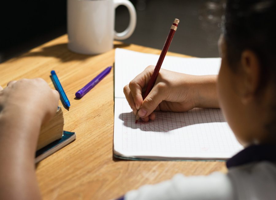 detailed view of a little latin girl's hands painting with her red pencil on her notebook, on top of a wooden desk. doing her homework.